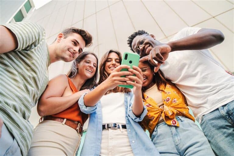 Eine Gruppe junger Menschen schaut lächelnd auf den Bildschirm eines Smartphones.